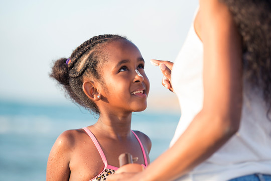 Image of mother applying sunscreen on child at the beach